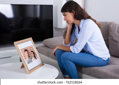 Sad Woman Holding Picture Frame Of Couple In Love At Home