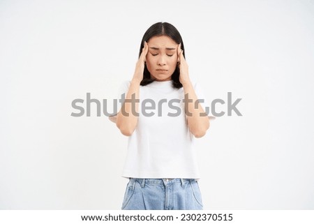 Sad woman holds hands on head, suffers headache, has migraine, feels dizzy, stands over white background.