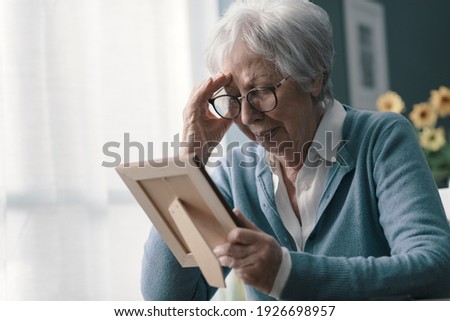 Sad woman at home grieving the loss of her husband, she is holding a picture and crying