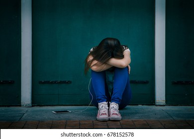 Sad Woman Hug Her Knee And Cry, Asian Woman In Light Blue Shirt And Jeans Sitting Against A Wall And Listening To Music