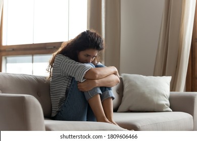 Sad woman hug knees sit on couch feels lonely goes through divorce or break up. Female with drug or alcohol addiction problem need rehab help. Unplanned pregnancy made decision about abortion concept