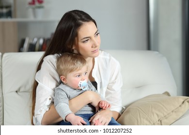 Sad Woman Looking Away With Her Baby Sitting On A Couch In The Living Room At Home