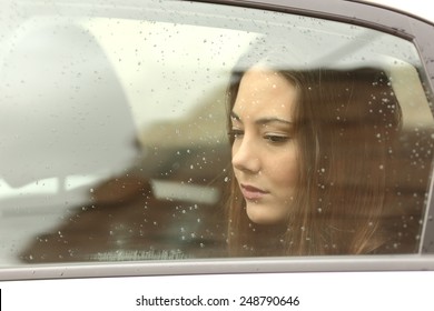 Sad Woman Looking Down Through A Car Window In A Rainy Day