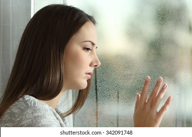 Sad woman looking the rain falling through a window at home or hotel