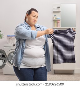 Sad Woman Looking At A Shrunken Shirt Inside A Bathroom