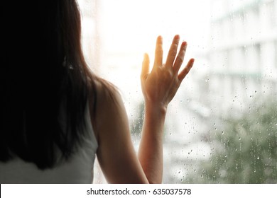Sad woman looking through the glass window with a rain drops on city background