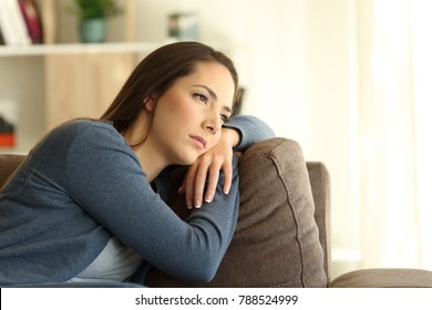 Sad woman looking trough a window sitting on a couch in the living room at home - Shutterstock ID 788524999
