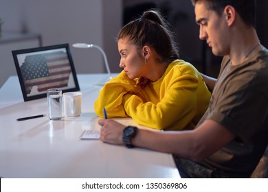 Sad Woman Looking At USA Flag In Picture Frame While Sitting With Her Military Boyfriend Who Is About To Leave For Deployment. 