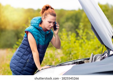 Sad woman looks under the hood of her car on the side of the road, talking on the phone. Traffic accident, car broke down. - Shutterstock ID 1825545266