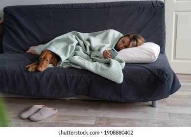 Sad Woman Lying On Sofa With Dog, Using Smart Phone In Hands Wait For Boyfriend Call Or Text, Feels Depressed. Thoughtful Female Think About Relationships Problems. Mental Health, Loneliness Concept.