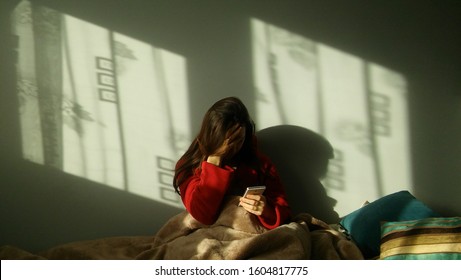 Sad woman making a phone call on the bed. Depressed, evastated woman sitting in bed and holding the phone