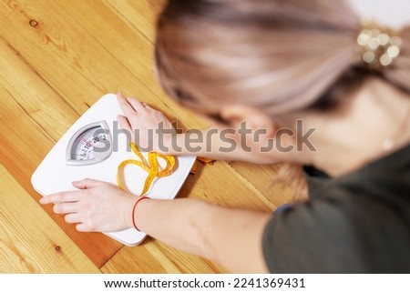 Sad woman with a measuring tape looks at a white scale on a wooden floor Imagine de stoc © 