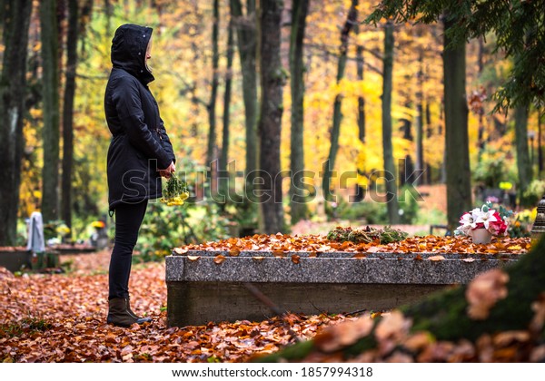 Sad woman is mourning for dead person at grave in\
cemetery. Lonely mourner in autumn graveyard.  Grief and cry for\
dead people