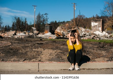 Sad woman owner holds his head by hand checking burnt out house and  yard after fire disaster, consequences of fire disaster accident. Ruins after fire disaster, loss and despair concept.