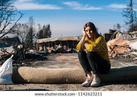 Sad woman owner holds his head by hand checking burnt out house and  yard after fire disaster, consequences of fire disaster accident. Ruins after fire disaster, loss and despair concept.