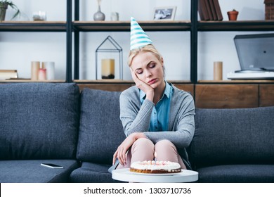 Sad Woman In Party Hat Propping Head With Hand While Celebrating Birthday At Home Alone