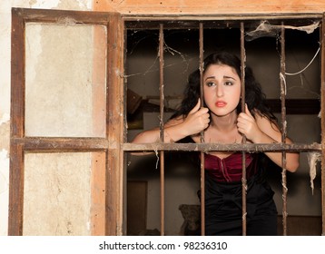 Sad Woman In Prison Behind Bars Of A Derelict Building