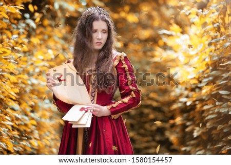 Sad woman in a red dress reading a letter in the autumn park