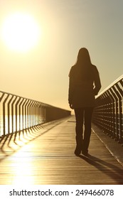 Sad woman silhouette walking alone on a bridge on the beach in winter at sunset