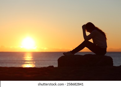 Sad Woman Silhouette Worried On The Beach At Sunset With The Sun In The Background