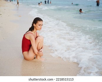 A Sad Woman Sits On The Sand On The Beach With Her Arms Around Her Legs Watching The Sun Set On A Tropical Island