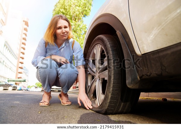 a sad woman sits at the\
punctured wheel of a car. tire service and car service on call.\
courses for drivers and car mechanics. pump for car wheels. solar\
glare 