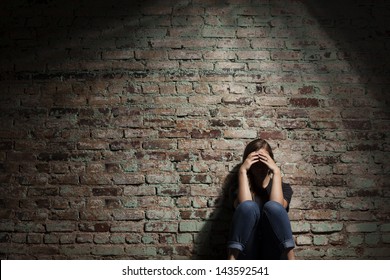 Traurige Frau sitzt allein auf Ziegelmauer.