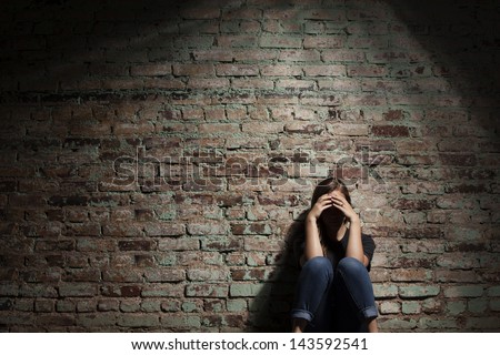 Sad woman sitting alone against brick wall.