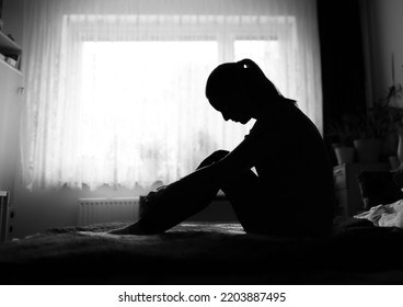 Sad Woman Sitting Alone At Home In Dark Bedroom	