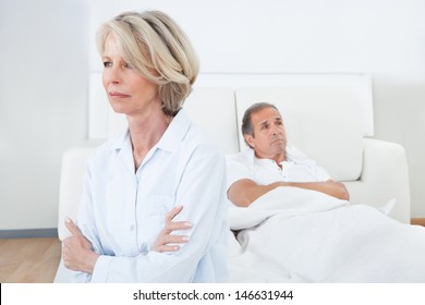 Sad Woman Sitting At The Edge Of Bed In Front Of Man - Powered by Shutterstock