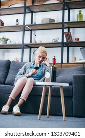 Sad Woman Sitting On Couch With Glass Of Red Wine And Tissue Box In Living Room