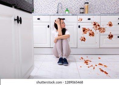 Sad Woman Sitting On Floor With Spilled Food In Kitchen