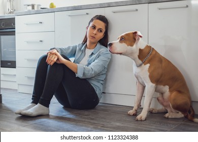 Sad Woman Sitting On A Kitchen Floor And Looking At Her Dog