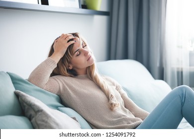 Sad woman sitting on sofa at home, thinking about important things