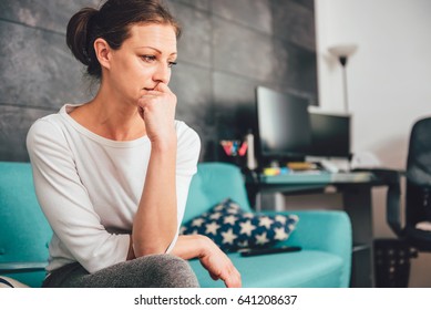 Sad woman sitting on a sofa in the living room - Shutterstock ID 641208637