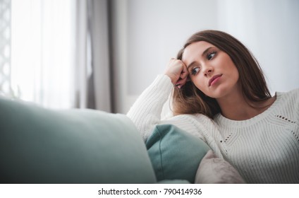 Sad Woman Sitting On Sofa At Home Deep In Thoughts, Thinking About Important Things