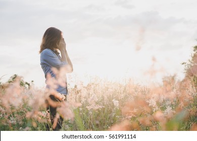Sad woman standing in field with sunset background.