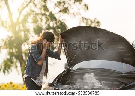sad woman standing on the road by the broken car in the middle of nowhere. smoke coming out the engine. Help needed. Car service. Tow service.