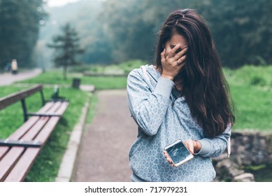 Sad Woman Standing In The Park With Cracked Phone