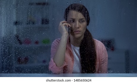 Sad Woman Talking Phone Behind Rainy Window, Shocked By Bad News From Family