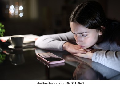 Sad woman waiting for a mobile phone call looking it in the night at home