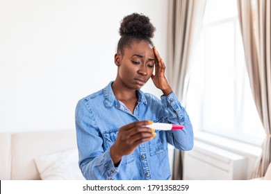 Sad, Worried African American Woman Checking Her Recent Pregnancy Test, Sitting On Couch At Home. Maternity, Child Birth And Family Problems Concept. Unwanted Pregnancy