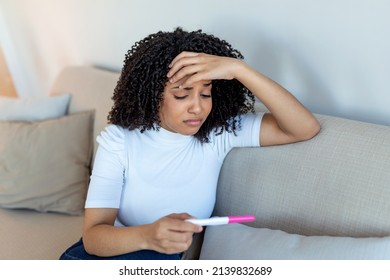 Sad, Worried African American Woman Checking Her Recent Pregnancy Test, Sitting On Couch At Home. Maternity, Child Birth And Family Problems Concept. Unwanted Pregnancy