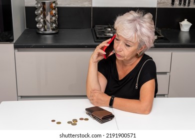 A sad and worried elderly woman is talking on a smartphone, there is a purse and small coins in front of her. Concept: poverty and lack of livelihood, rising prices.