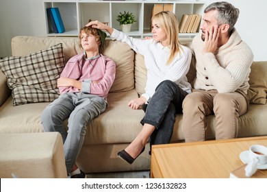 Sad Worried Parents In Casual Outfit Puzzled About Depression Of Teenage Son Who Ignoring Them, Disappointed Mother Stroking Head Of Son In Living Room