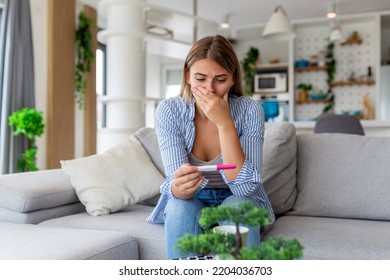 Sad, Worried Woman Checking Her Recent Pregnancy Test, Sitting On Couch At Home. Maternity, Child Birth And Family Problems Concept. Unwanted Pregnancy