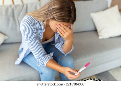 Sad, Worried Woman Checking Her Recent Pregnancy Test, Sitting On Couch At Home. Maternity, Child Birth And Family Problems Concept. Unwanted Pregnancy