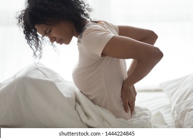 Sad Young African Woman Touching Back Feeling Backache Morning Discomfort Low Lumbar Muscular Kidney Pain Sit On Bed After Bad Sleep Waking Up On Uncomfortable Mattress Bending From Backpain Concept