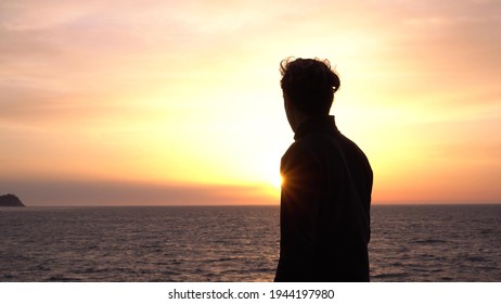 Sad Young Alone Man Looks Thoughtfully At The Ocean. Beautiful Sunrise Background. Travel And Self-isolation, Social Distancing. Nature, Sea, Beach, Morning