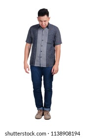 Sad young Asian man wearing blue jeans and batik shirt looking down. Isolated on white. Full body portrait